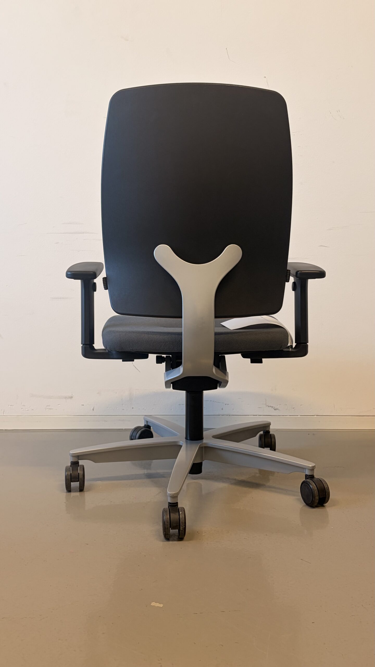 Bürostuhl mit hellrosa Rückenlehne, grauem Sitz und schwarzen Armlehnen vor weißer Wand hinten