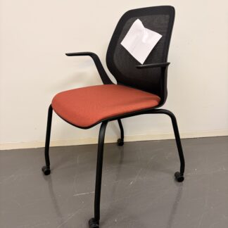 Bürostuhl mit schwarzem Netzrücken, roten Sitzpolster, schwarzen Armlehnen und vier Rollen schräg